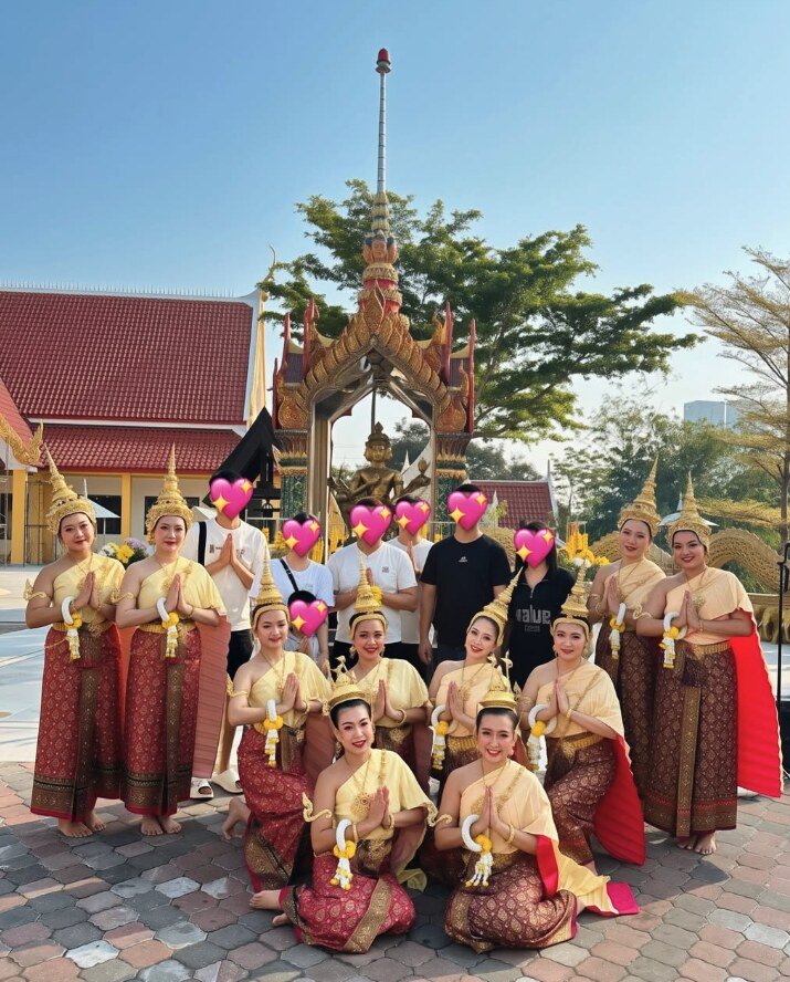 Thai dancers in red and gold costumes giving a wai greeting with guests in front of a golden shrine at a blessing ceremony